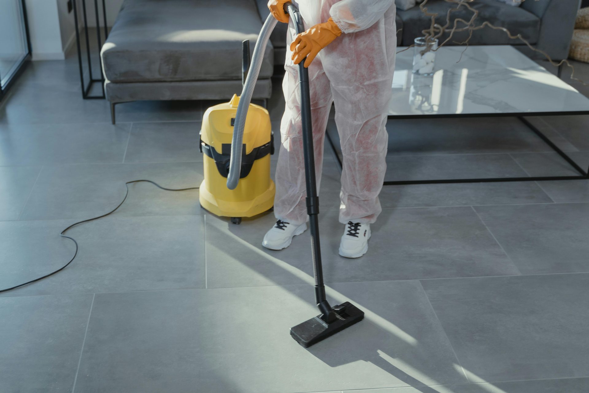 Worker vacuuming floor in modern living room.